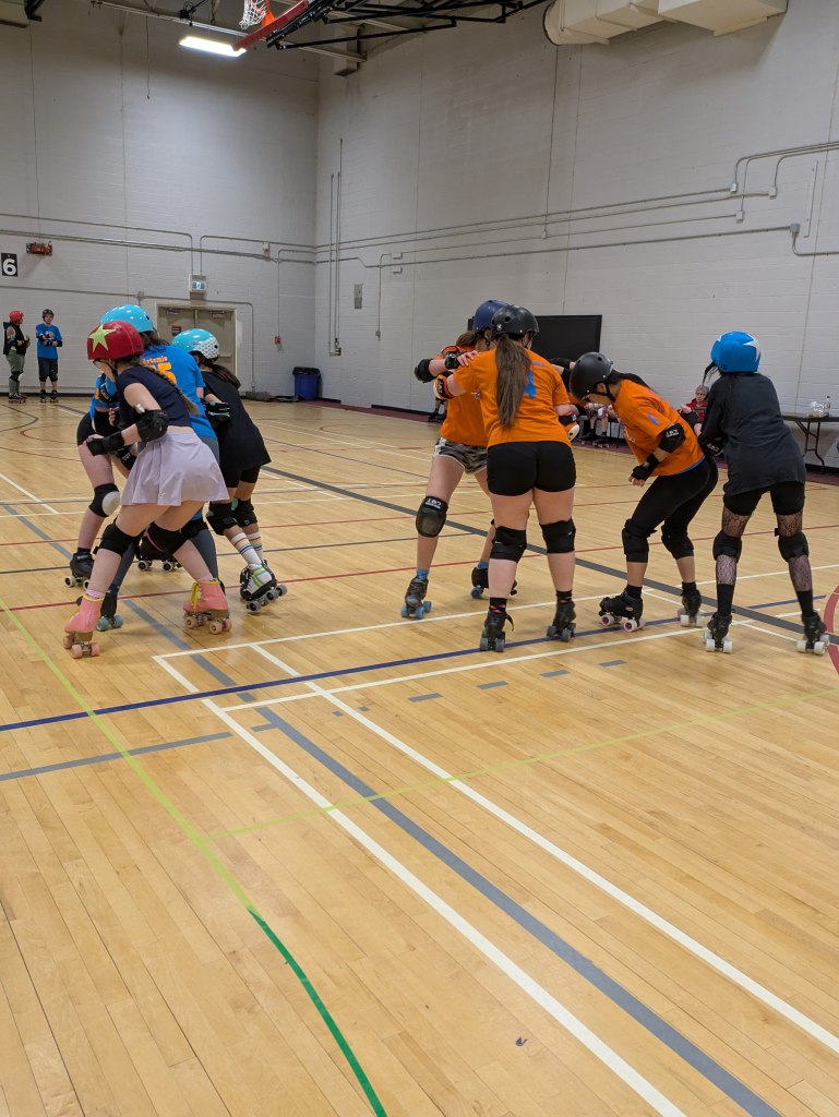 Youth playing roller derby in a gym.