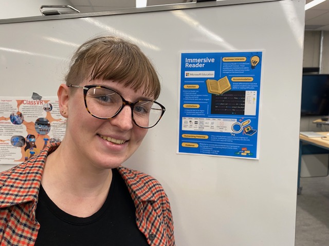 Me standing next to a large poster board presentation about the accessibility features of Immersive Reader software.