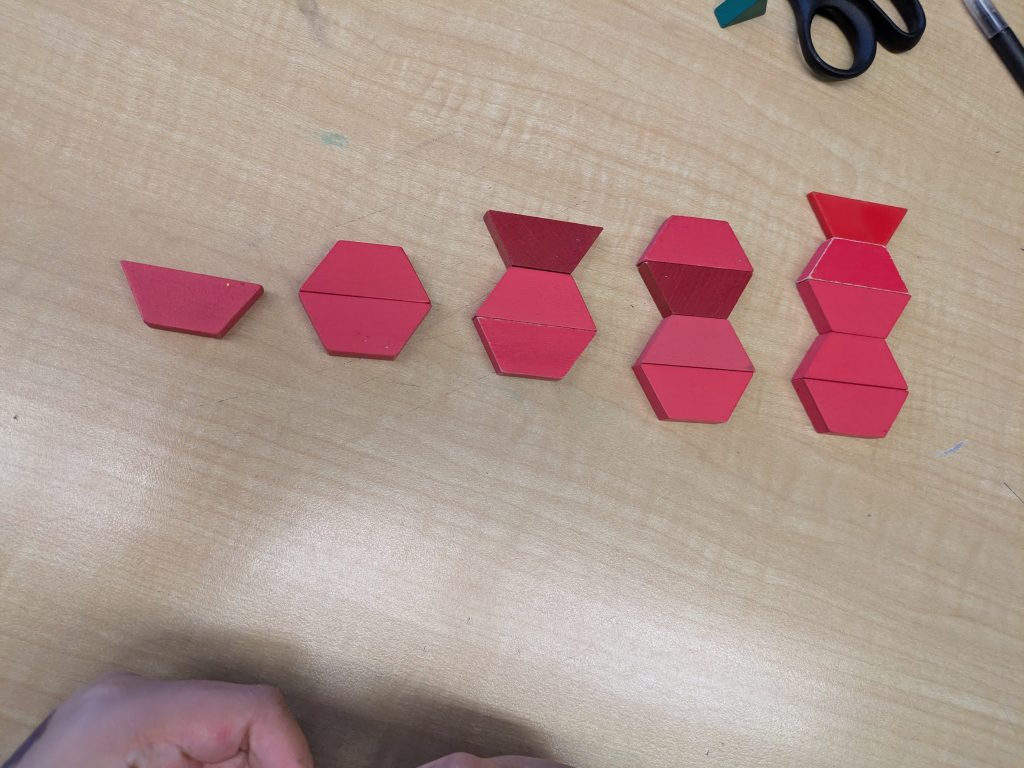 A growing geometric pattern created on a desk using red trapezoid math manipulatives.