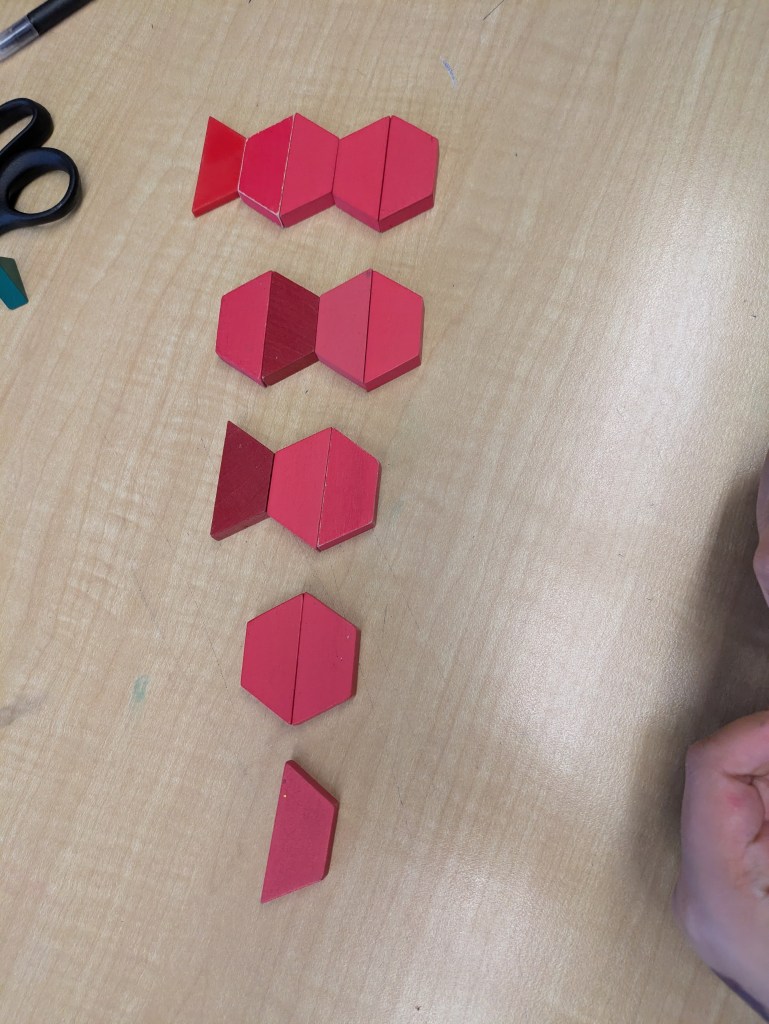 A growing geometric pattern created on a desk using red trapezoid math manipulatives.