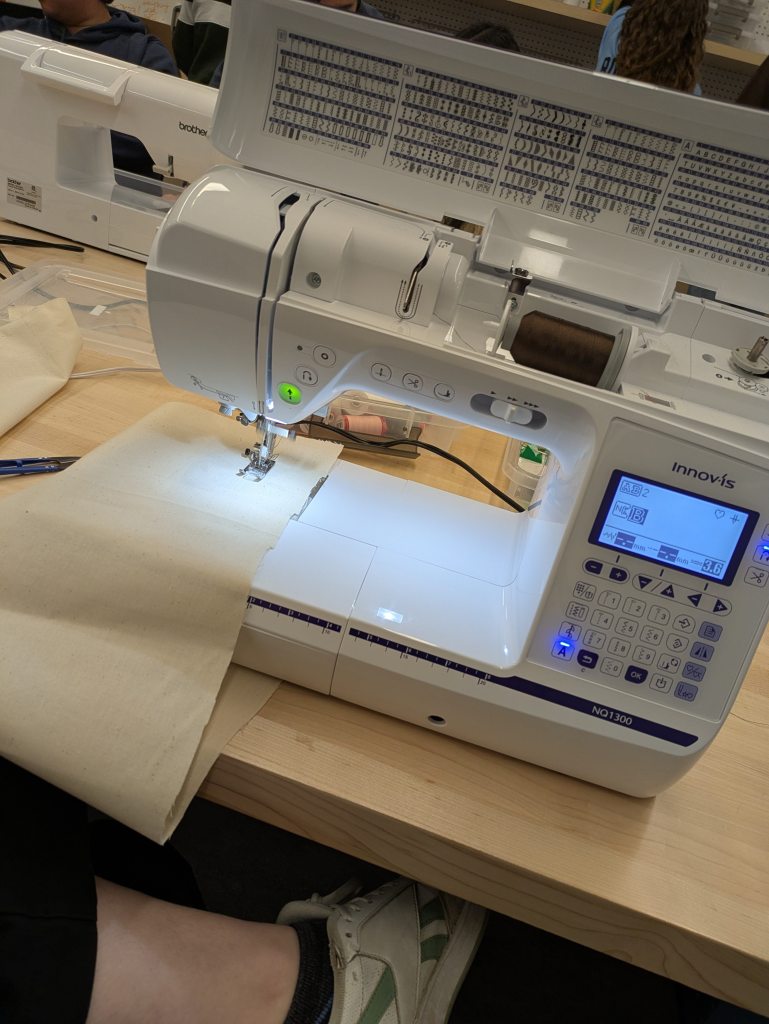 A close-up of a high-tech sewing machine automatically embroidering a design in a university Education Makerspace.