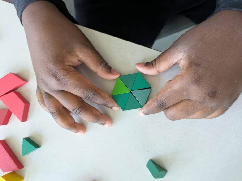 Pattern blocks arranged on a table, showing green triangles forming a yellow hexagon.