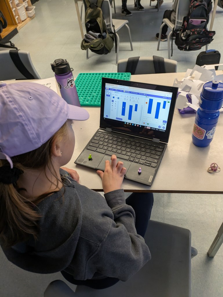 A student's hand on a mouse, focused on a computer screen running the Scratch block-coding interface.